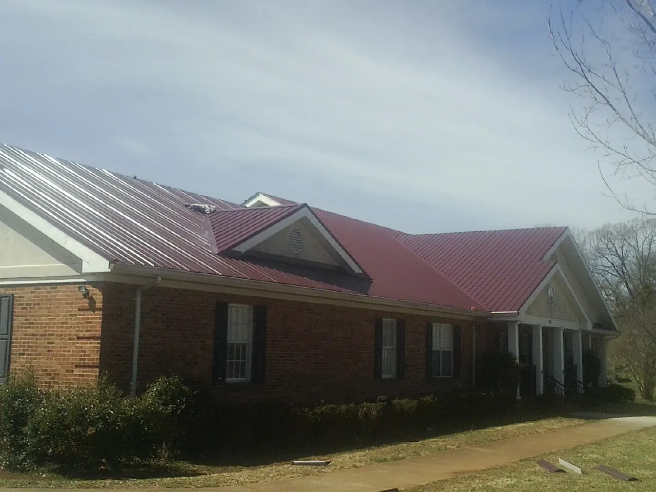 Red metal roof with gabled entries on a long brick building, from a Hail Damage Roof Repair job in Dumont