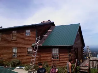 Green metal roof going on a two story log home with ladders set in Dumont